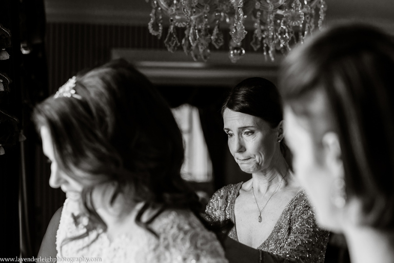 The mother of the bride holds back her tears as she buttons up her daughter's wedding dress