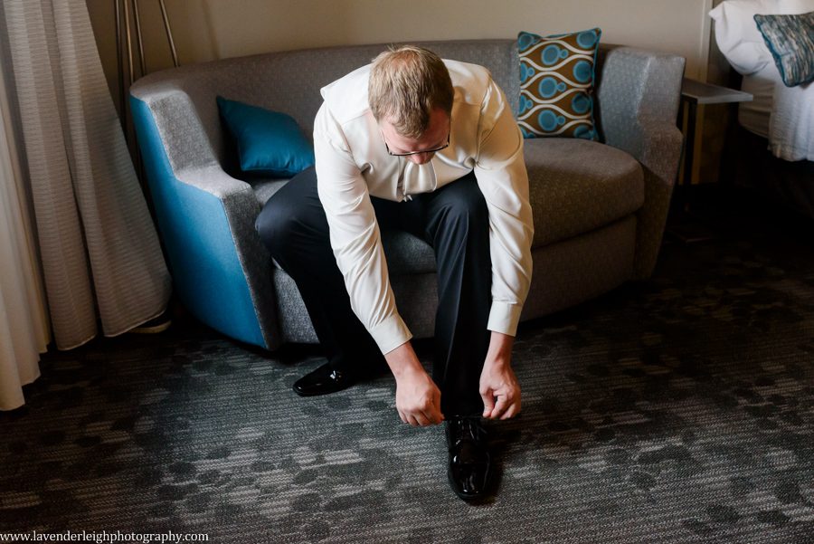 Groom Ties Shoe as He Gets Ready for Wedding at the Courtyard Marriott Settler's Ridge