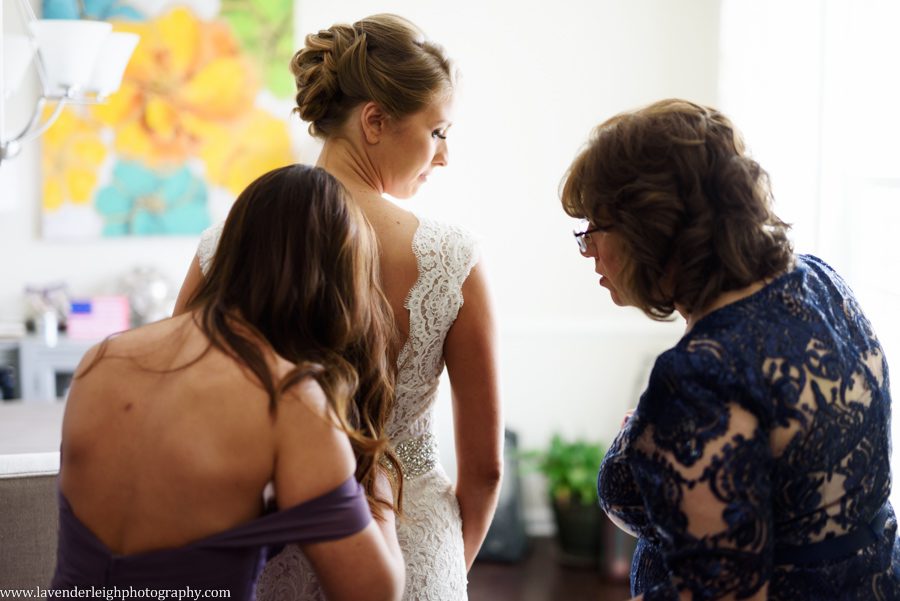 The maid of honor and mother of the bride help to button the wedding dress