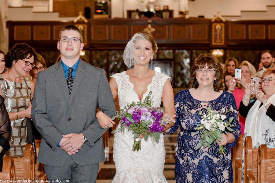 A bride walks down the aisle on her wedding day with her mother and brother