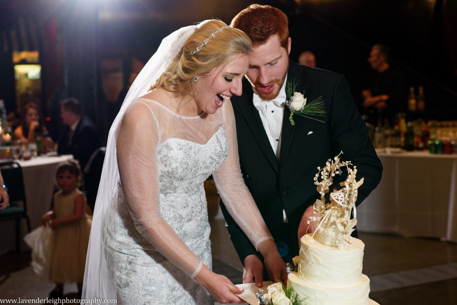 A bride and groom laugh as they attempt to cut their wedding cake