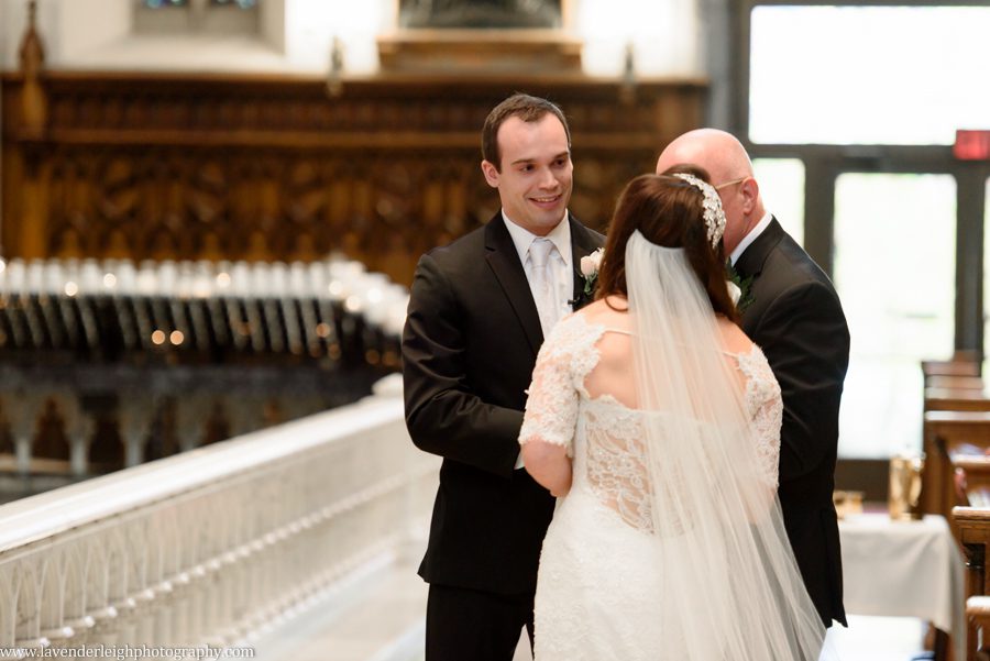 The groom smiles as his bride is handed off to him at a wedding ceremony at St. Paul Cathedral in Pittsburgh, Pennslyvania