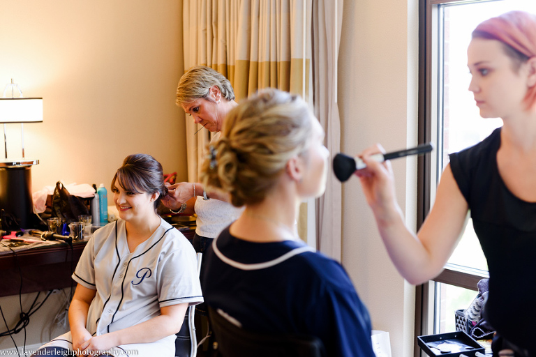 The bride and a bridesmaid get their hair and makeup done on a wedding day.