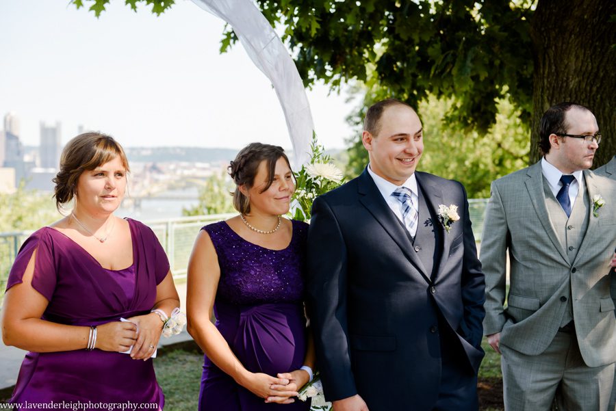 The groom watches his bride walk down the aisle at their wedding ceremony at the West End Overlook in Pittsburgh, Pennsylvania
