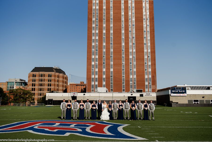 The bride, groom, and their wedding party pose for a picture on the Duquesne University football field