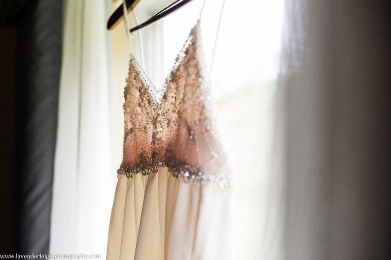 An elegant empire-waist wedding dress hanging in a hotel window.