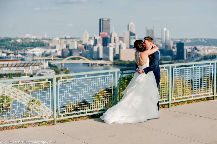 The bride and groom kiss in front of the city skyline at The West End Overlook in Pittsburgh, Pennsylvania
