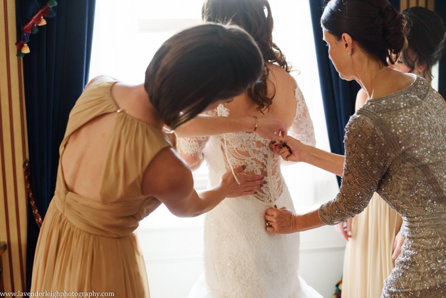 The mother of the bride and maid of honor button the bride's wedding dress after she puts it on