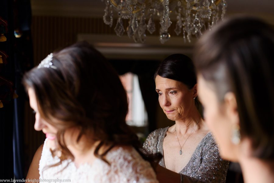 The mother of the bride tears up as she zips her daughter's wedding dress