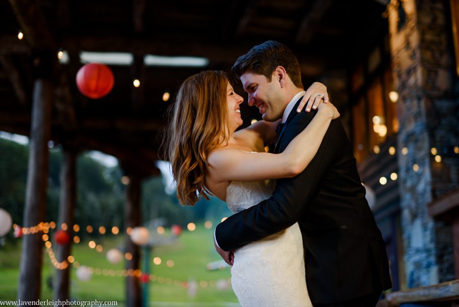 The bride and groom on a deck with twinkle lights overhead.